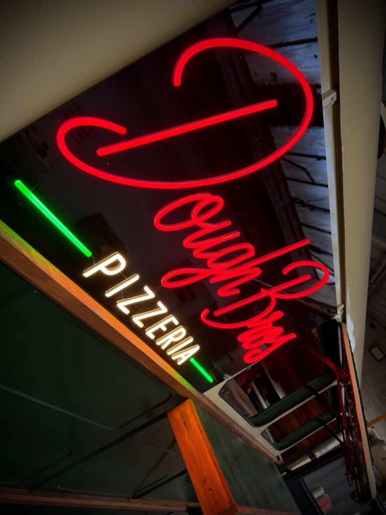 The red Dough Bros neon and warm-white Pizzeria sign above the trailer hatch
